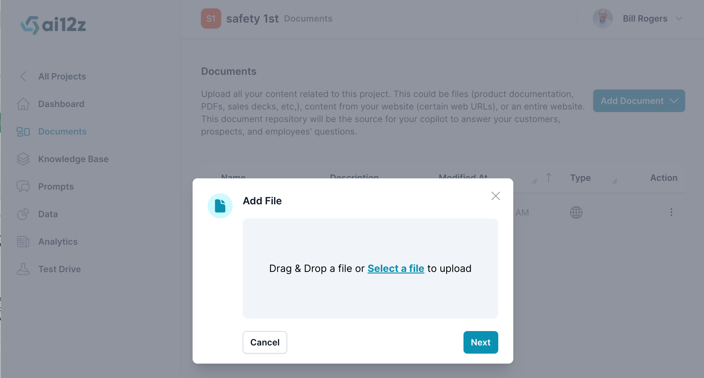 The image features a file upload interface within the ai12z platform. A popup window titled &#39;Add File&#39; is prompting the user to &#39;Drag &amp; Drop a file or Select a file to upload&#39;. There are &#39;Cancel&#39; and &#39;Next&#39; buttons at the bottom of the popup, indicating the steps to proceed with the file upload process. In the background, the &#39;Documents&#39; tab is highlighted in the sidebar, and there&#39;s a description that this area is for uploading content related to a project, such as files or entire websites. The interface is overlaid on a blurred background of the &#39;Documents&#39; section, indicating an interruption in the workflow to add a new document.